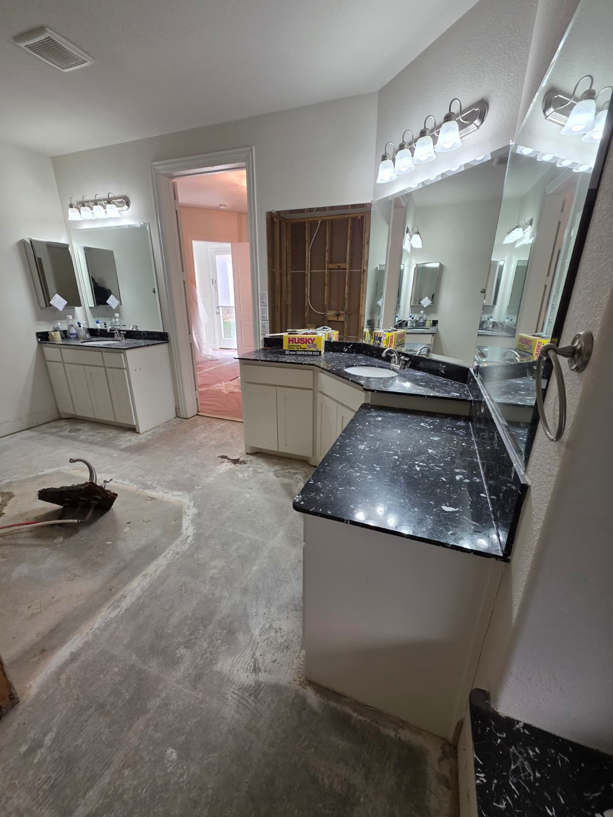 Dated bathroom with black granite counters, builder-grade mirrors and bare concrete floor