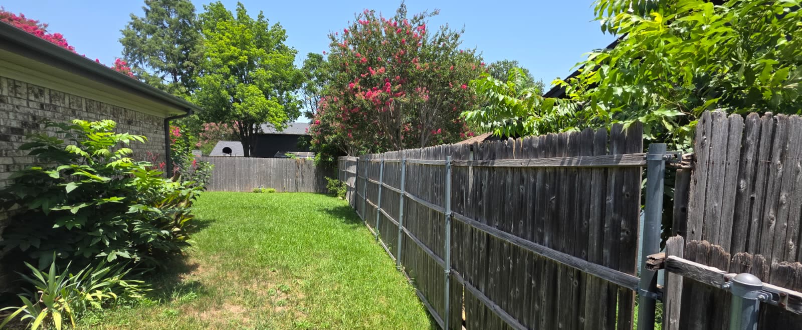 Old grey leaning wood fence propped up with metal posts along a backyard